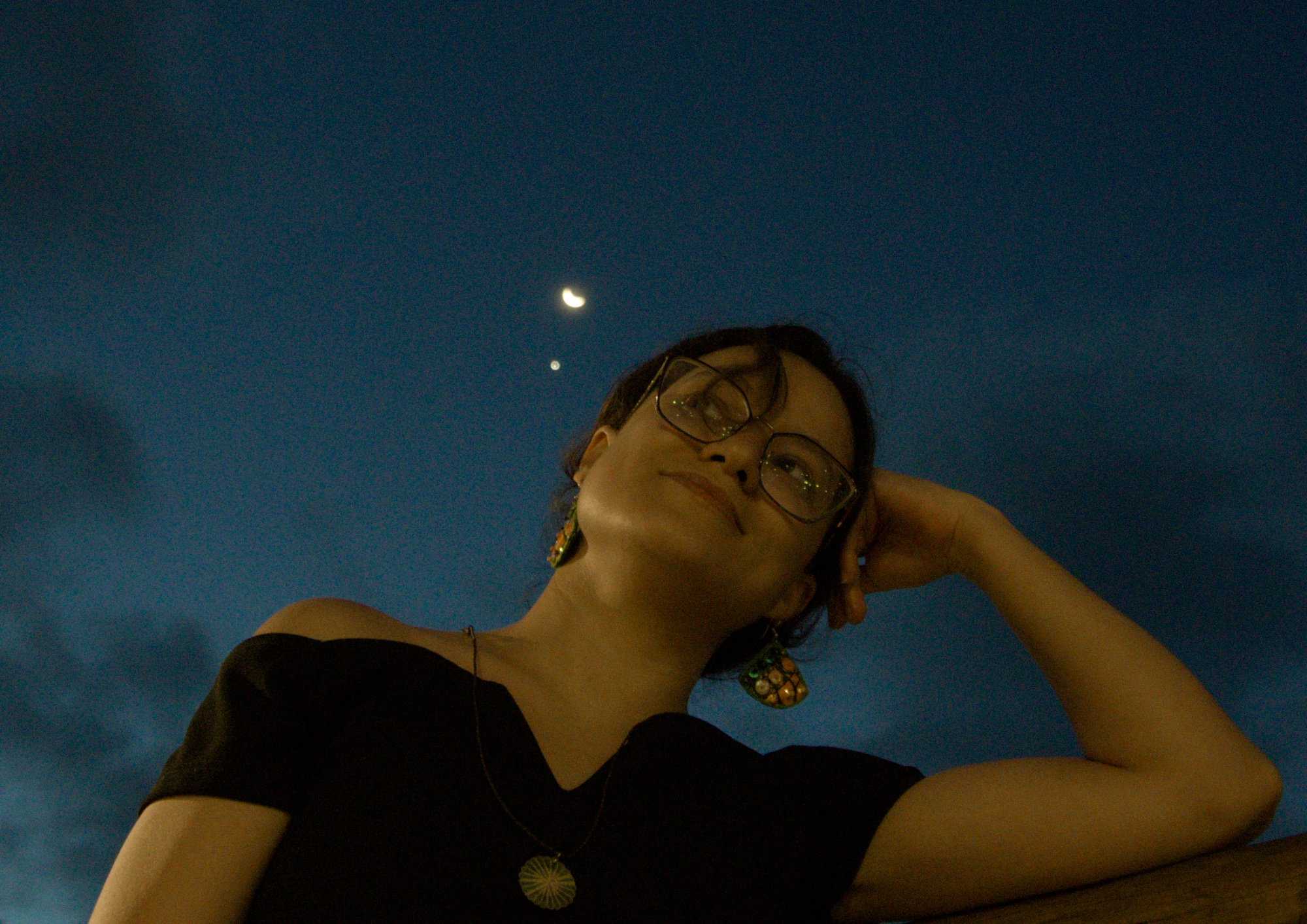 Mulher sorrindo contra a noite. A lua e vênus ao fundo, próximo ao seu rosto.